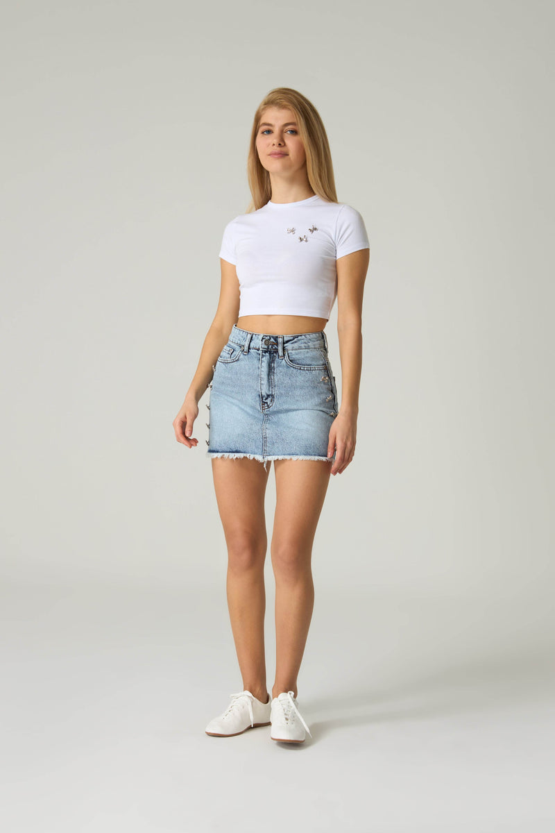 Woman wearing a white crop top and denim skirt on a plain background.