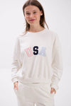 Woman wearing a white sweatshirt with 'USA' in colorful letters on a white background.