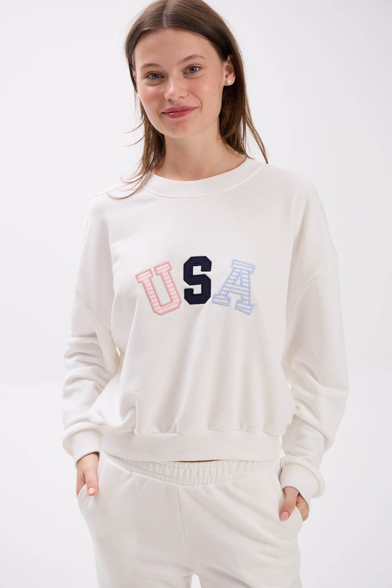 Woman wearing a white sweatshirt with 'USA' in colorful letters on a white background.