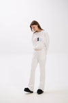 Person wearing a white sweatshirt with colorful text and white pants on a white background.