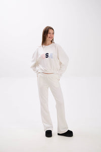 Person wearing a white sweatshirt and pants with a logo on a white background.