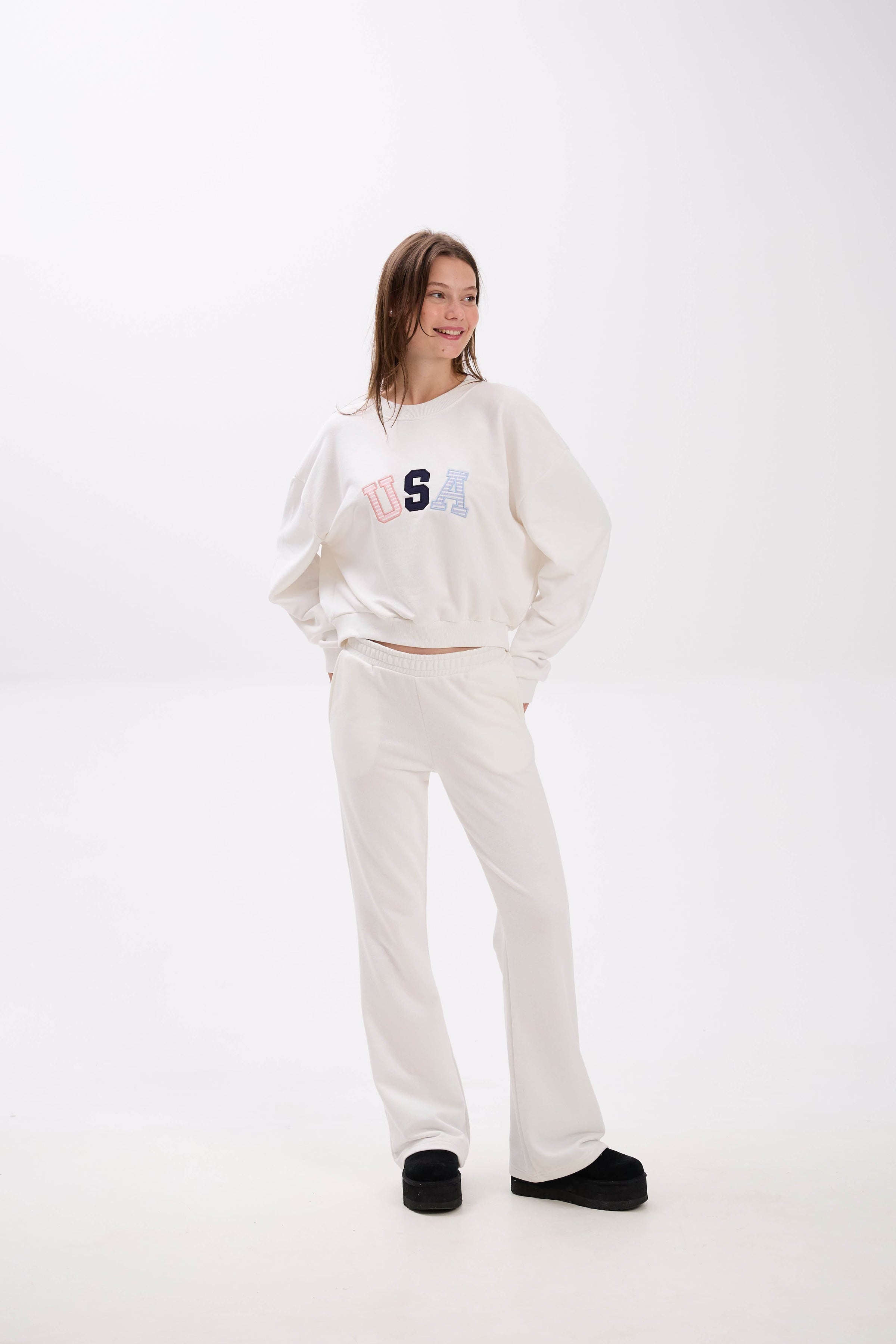 Person wearing a white sweatshirt and pants with a logo on a white background.