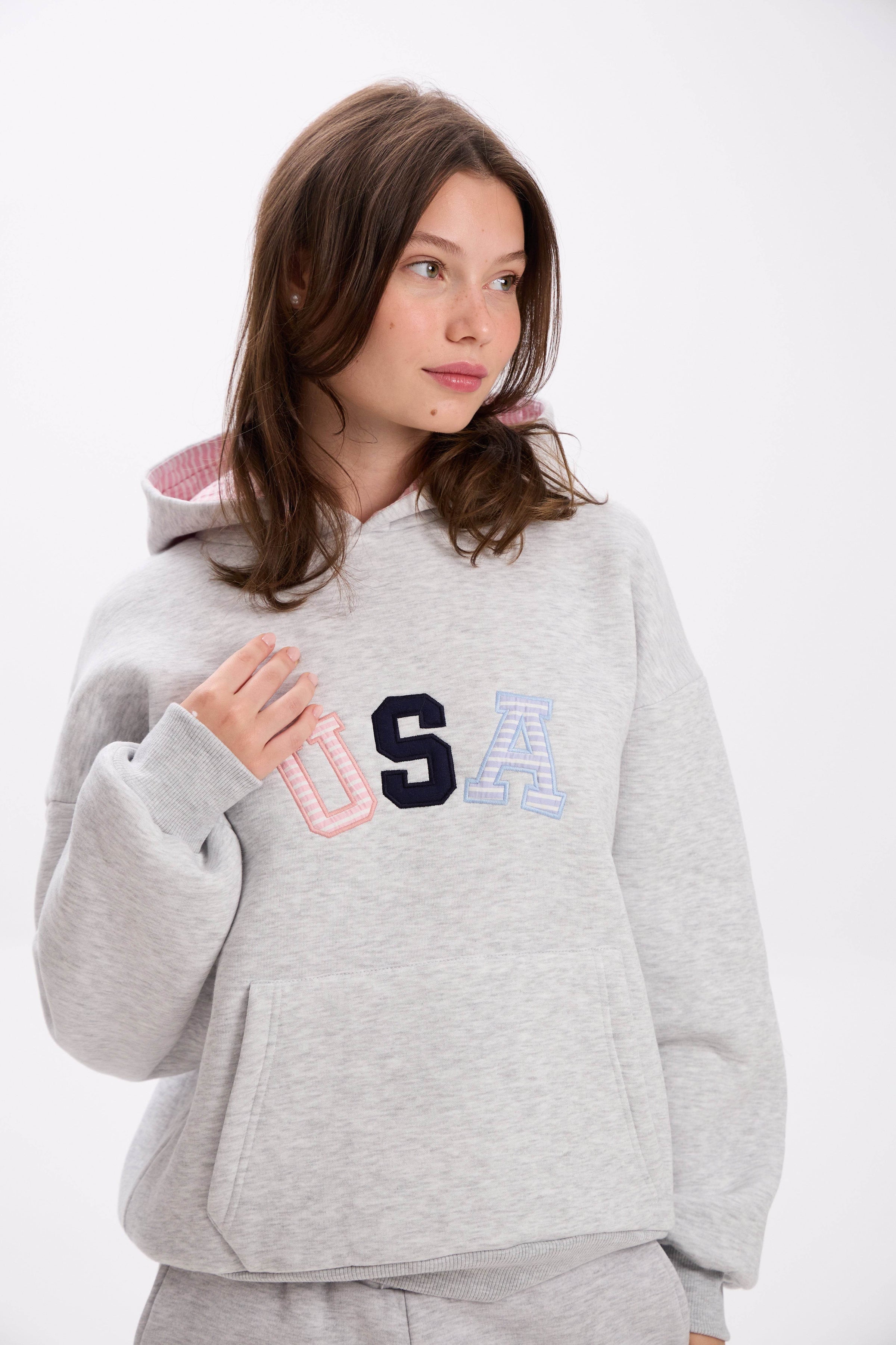 Woman wearing a gray hoodie with 'USA' letters in different colors on a white background.