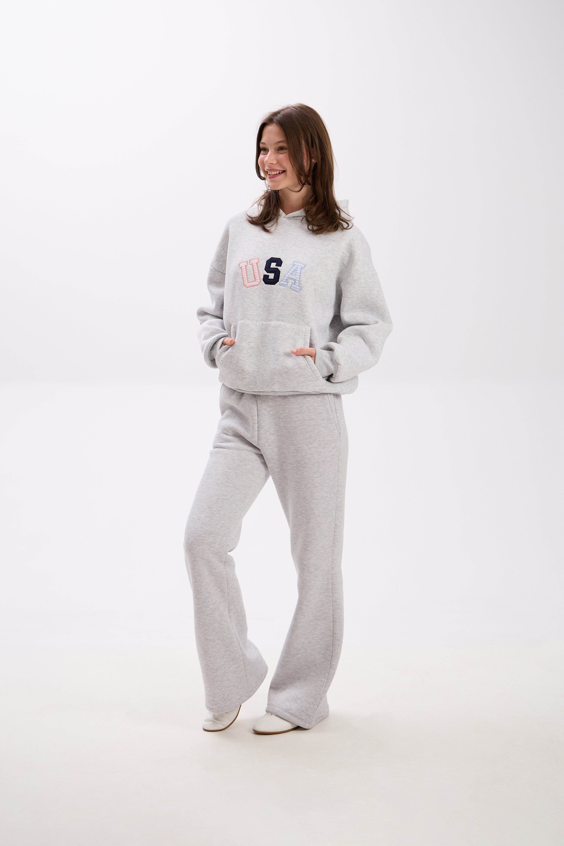Woman wearing a gray hoodie and pants with colorful text on a white background.