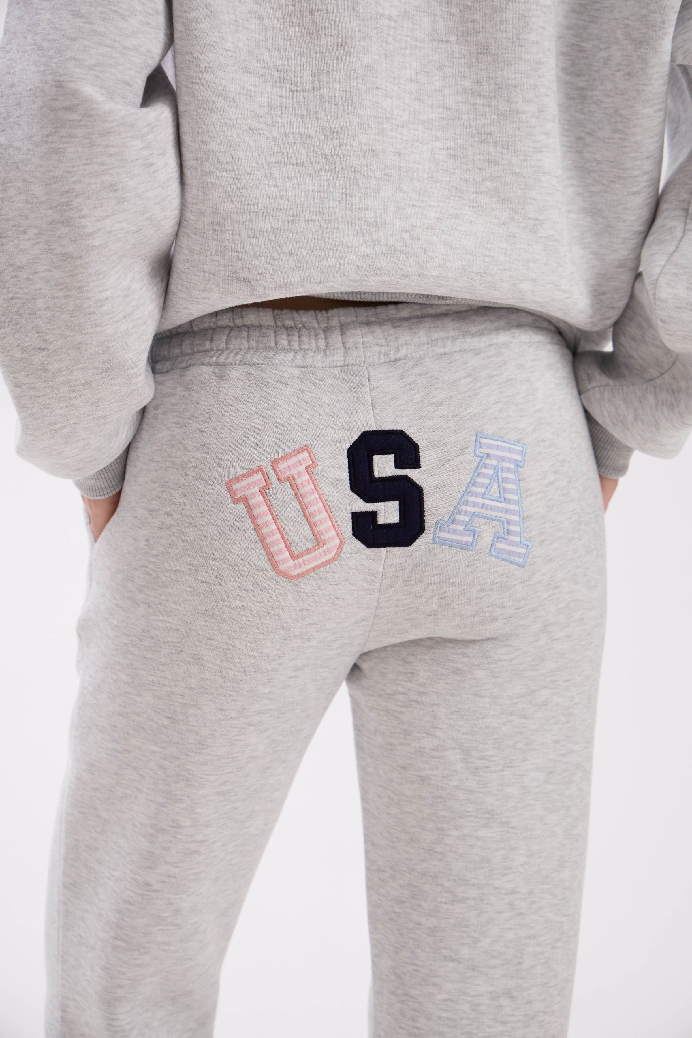 Grey sweatpants with elastic waistband, side pockets, and multicolor USA embroidery on the back.
