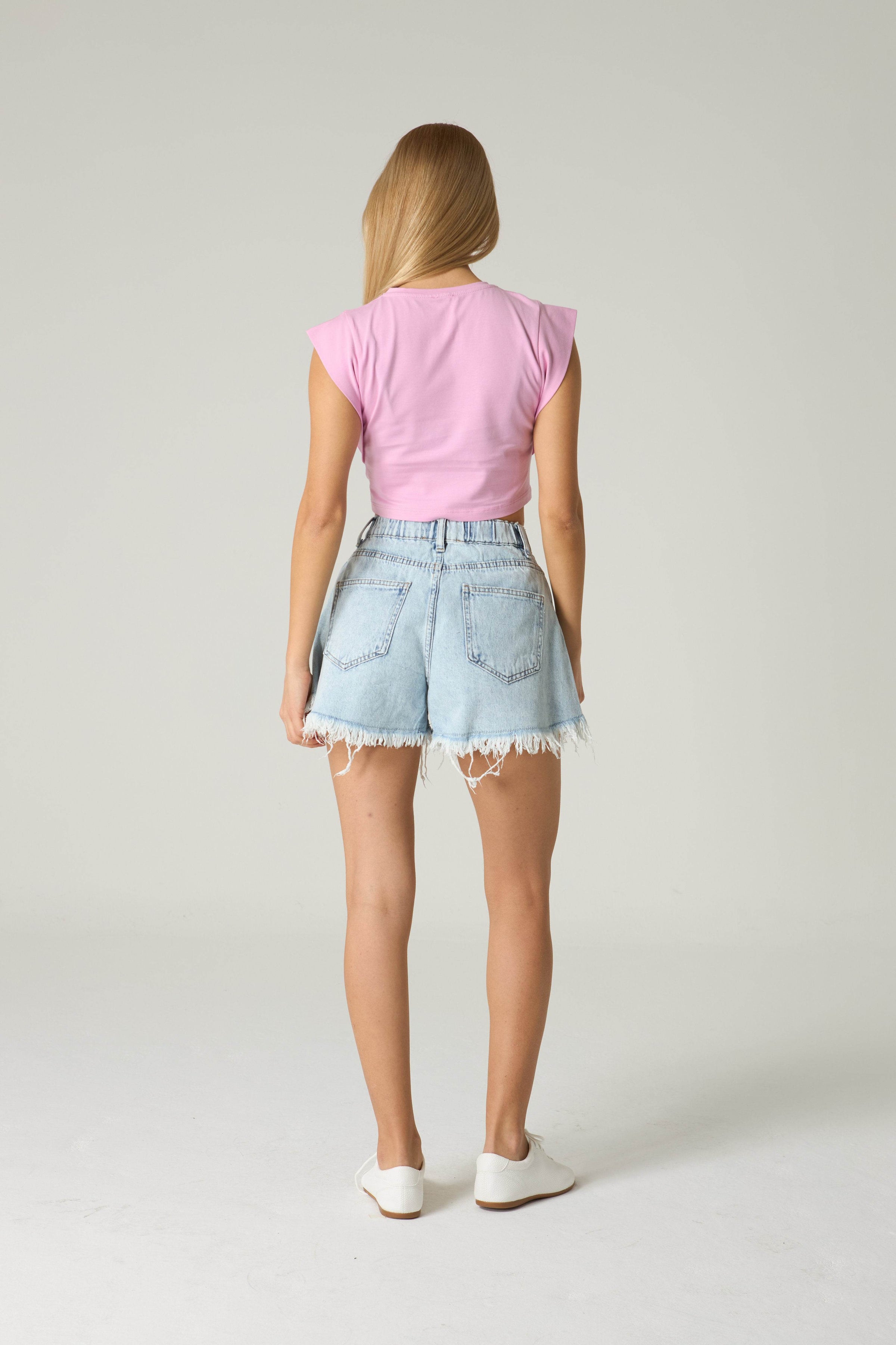 Person wearing a pink top and light blue denim shorts on a plain background.