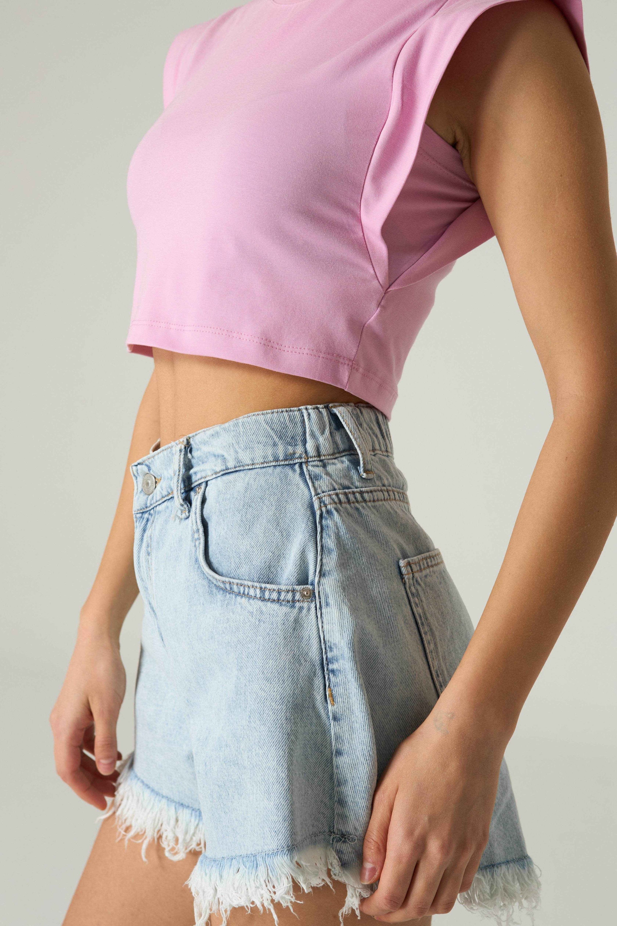 Person wearing a pink crop top and light blue denim shorts on a plain background.