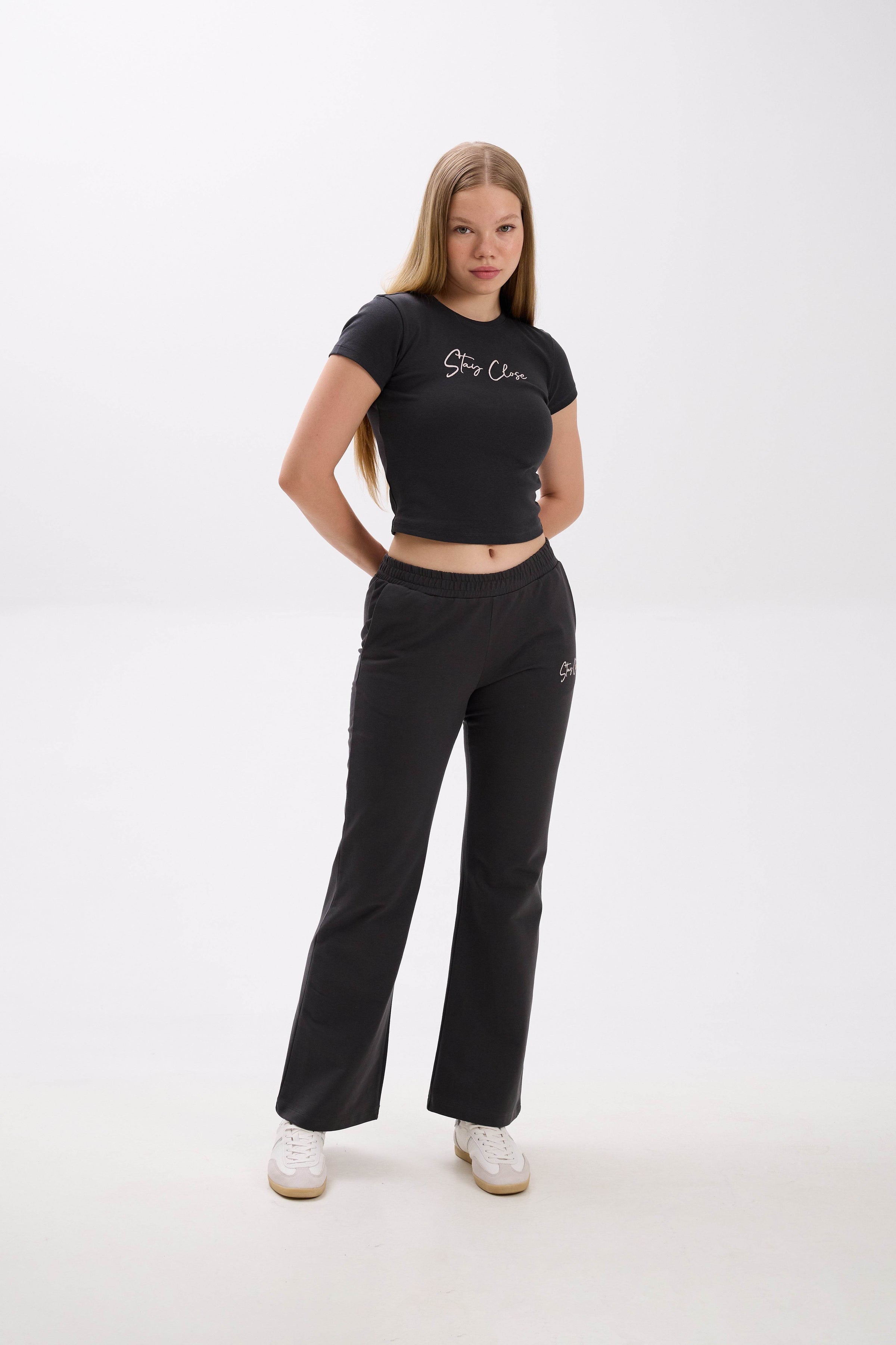Woman wearing a black crop top and pants with a "Stay Close" embroidery on a white background.