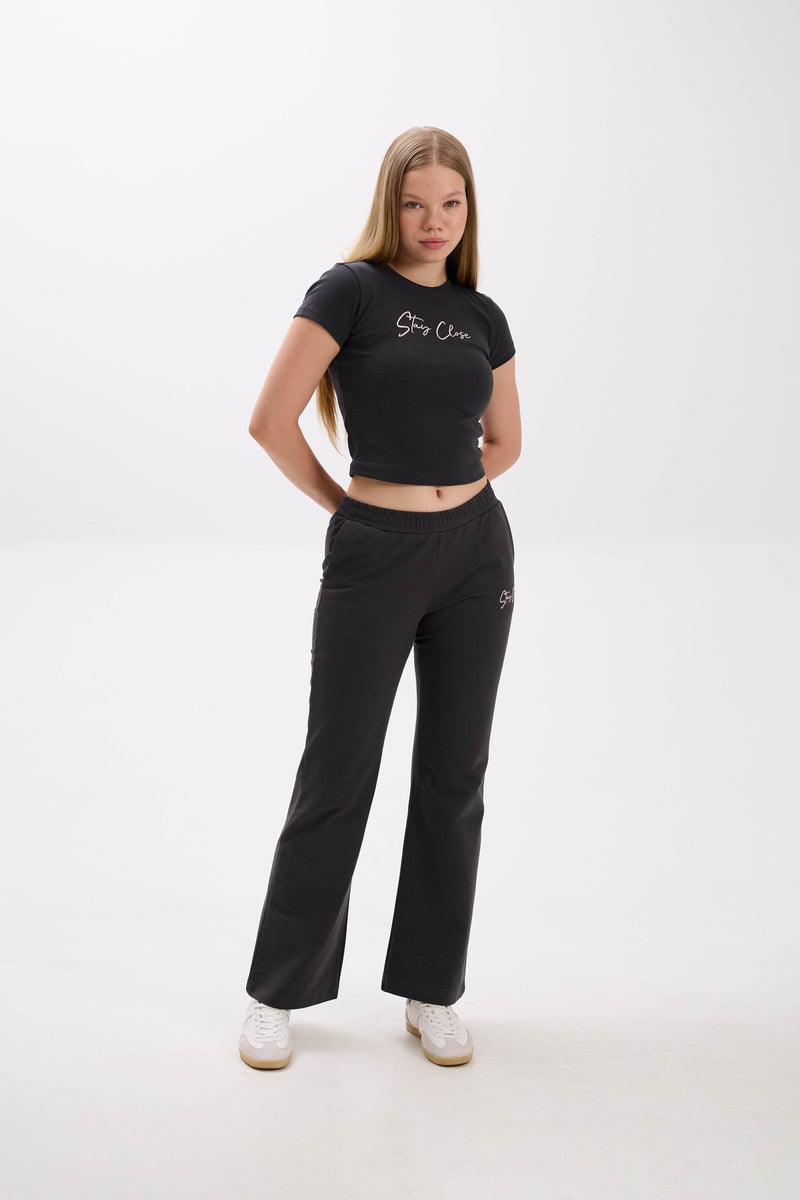 Woman wearing a black crop top and pants with a "Stay Close" embroidery on a white background.