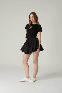 Woman wearing a black t-shirt with a graphic design and a black skirt on a white background.