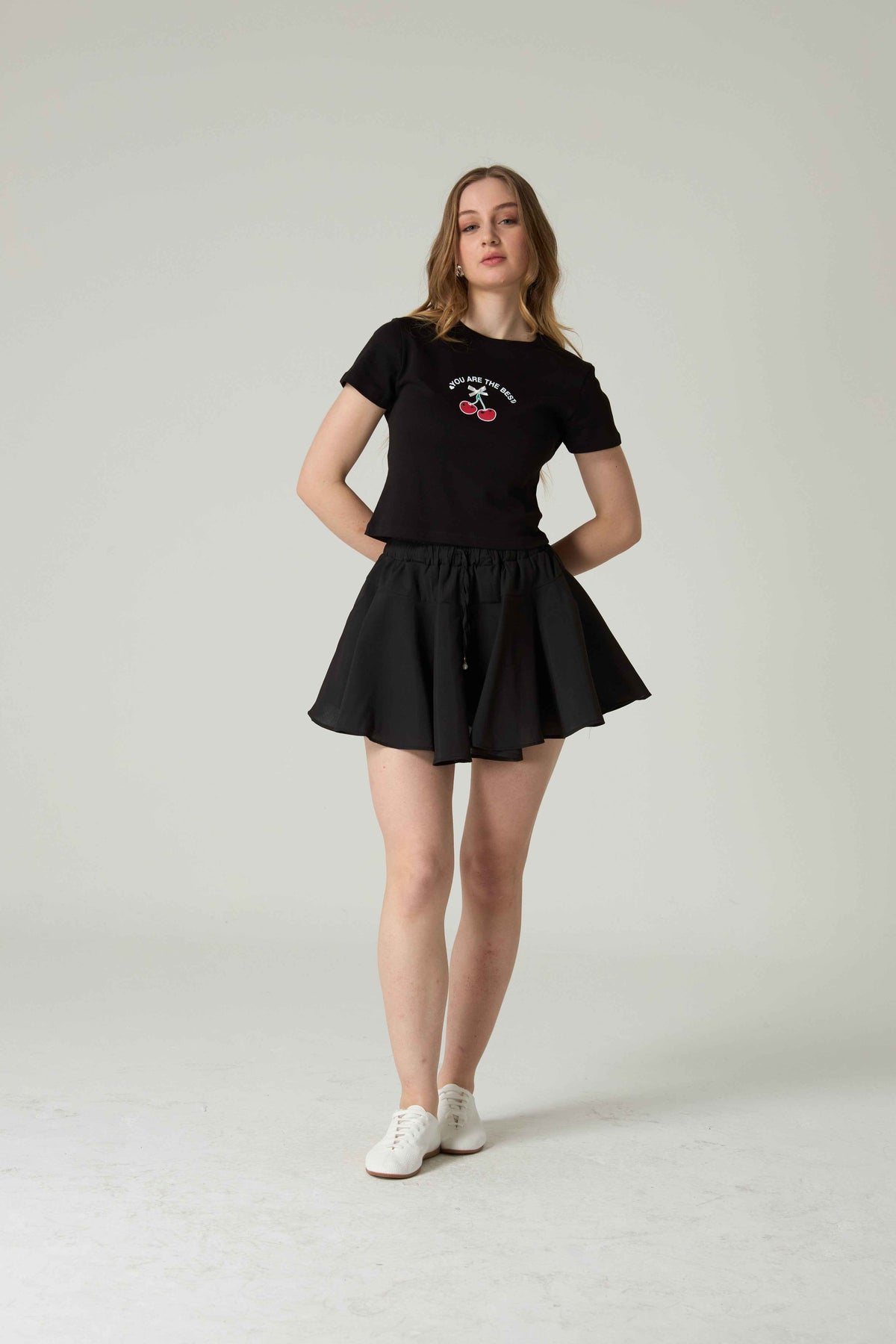 Person wearing a black t-shirt and skirt set on a plain background.