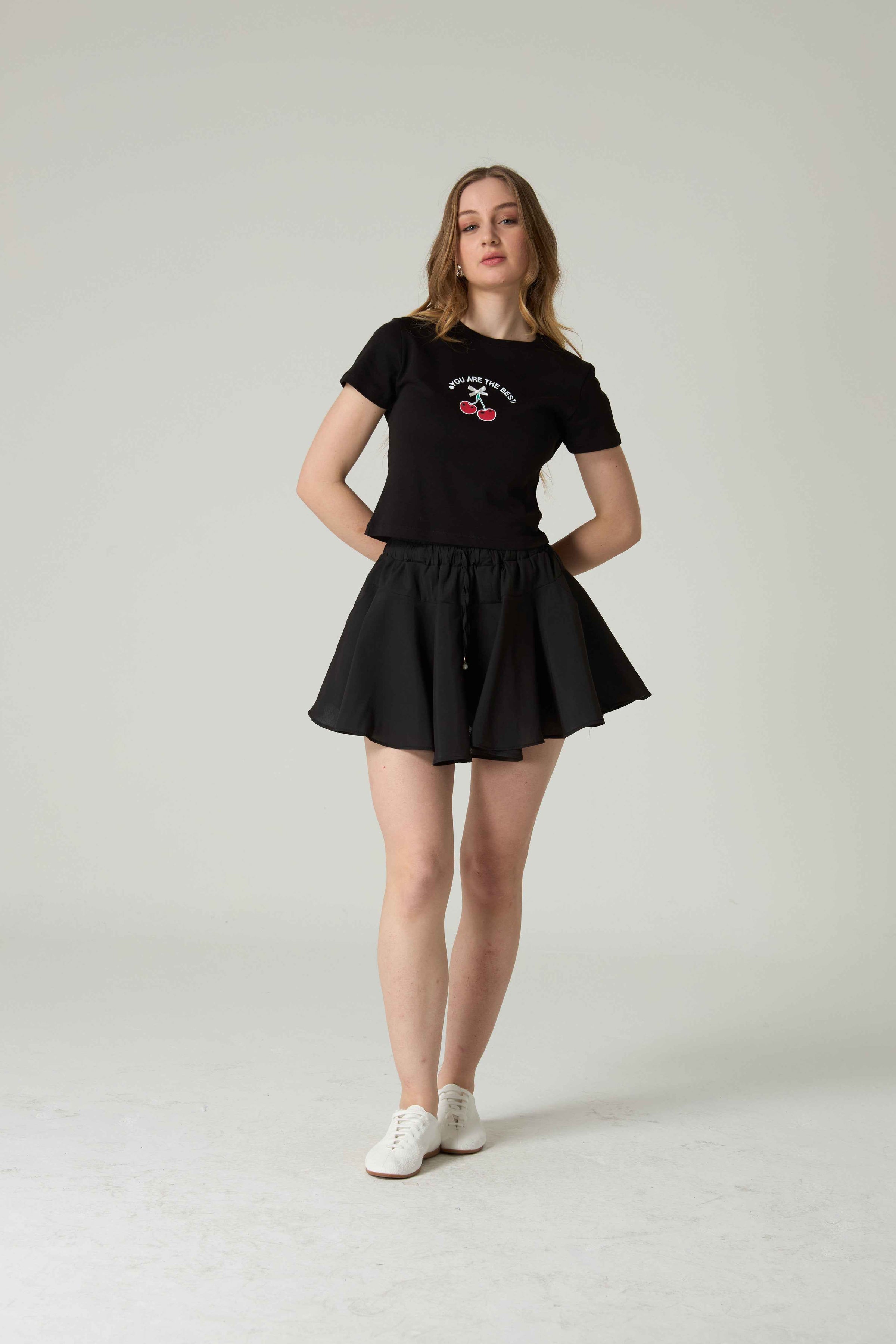 Person wearing a black t-shirt and skirt set on a plain background.