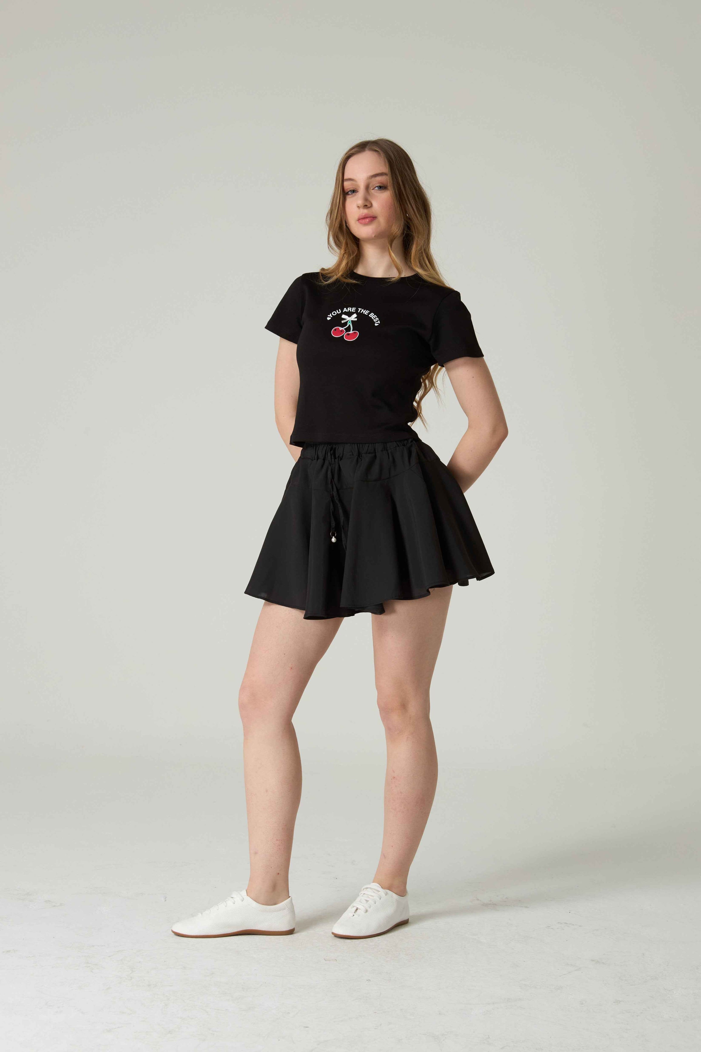 Woman wearing a black t-shirt with a graphic design and a black skirt on a white background.