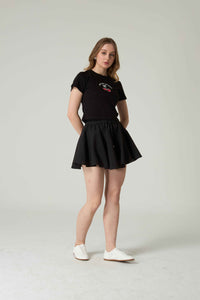 Woman wearing a black t-shirt with cherry embroidery and skirt on a plain background.
