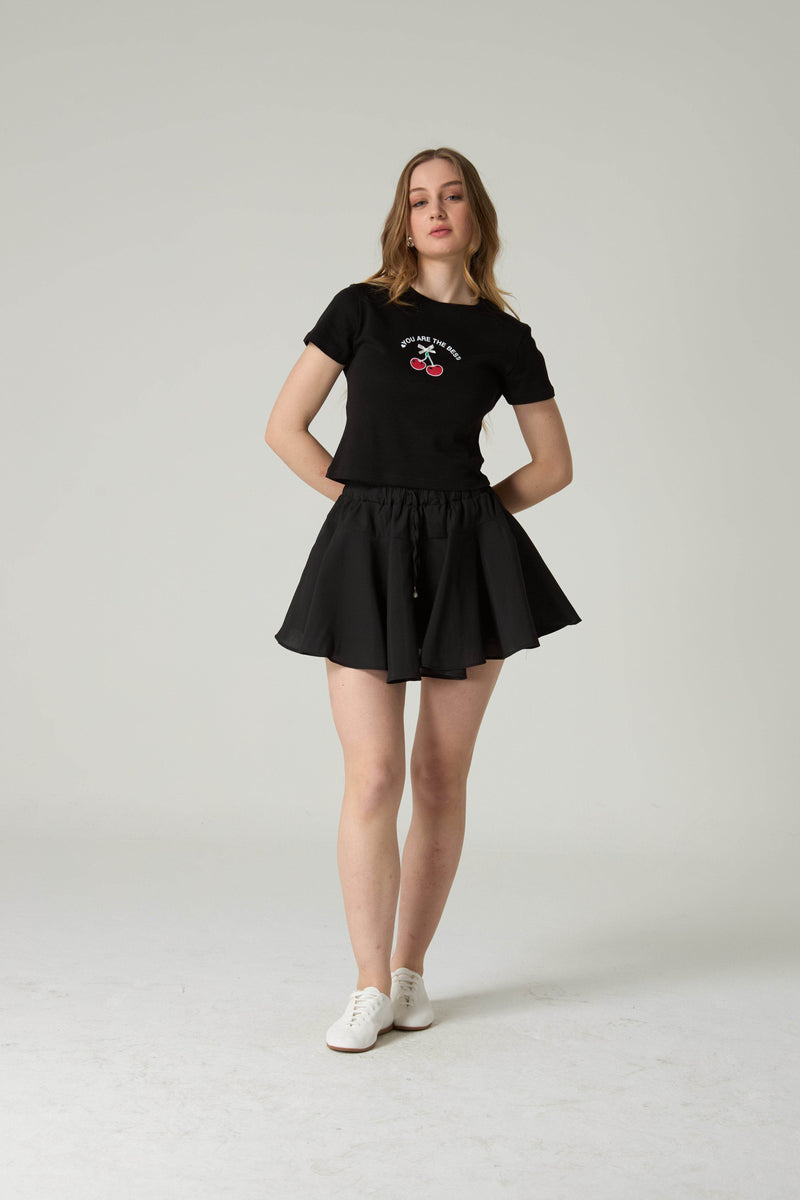 Woman wearing a black t-shirt and skirt set on a plain background.
