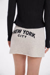 Person wearing a black sweater and grey melange / beige skirt with 'New York City' text on a white background