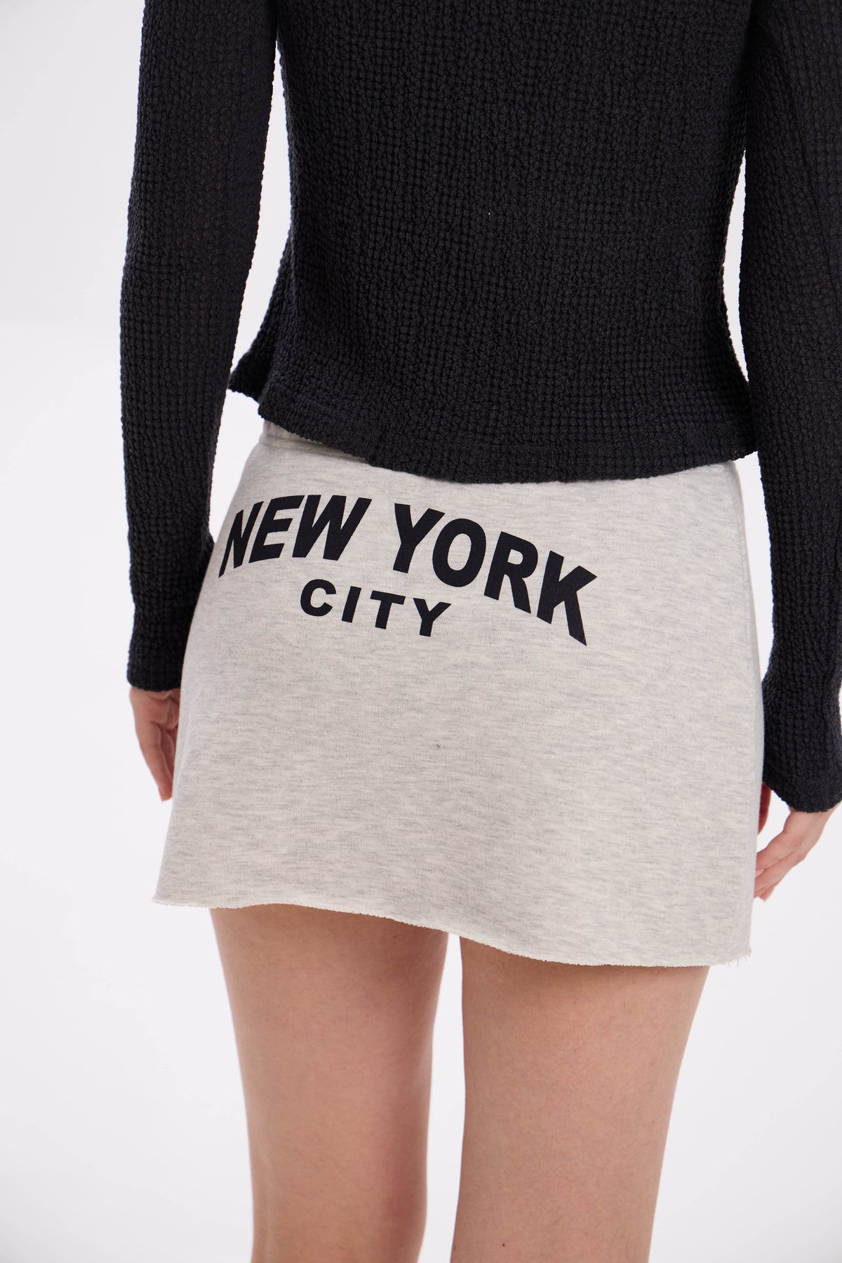 Person wearing a black sweater and grey melange / beige skirt with 'New York City' text on a white background