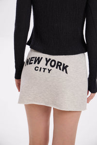 Person wearing a black sweater and grey melange / beige skirt with 'New York City' text on a white background