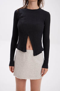 Person wearing a black long-sleeve top with a cutout design and a gray melange / beige skirt on a white background