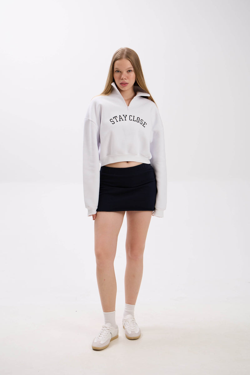 Person wearing a white hoodie with 'STAY CLOSE' text and a navy/black skirt on a white background