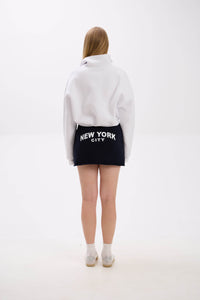 Person wearing a white hoodie and black skirt with 'New York City' text on a white background