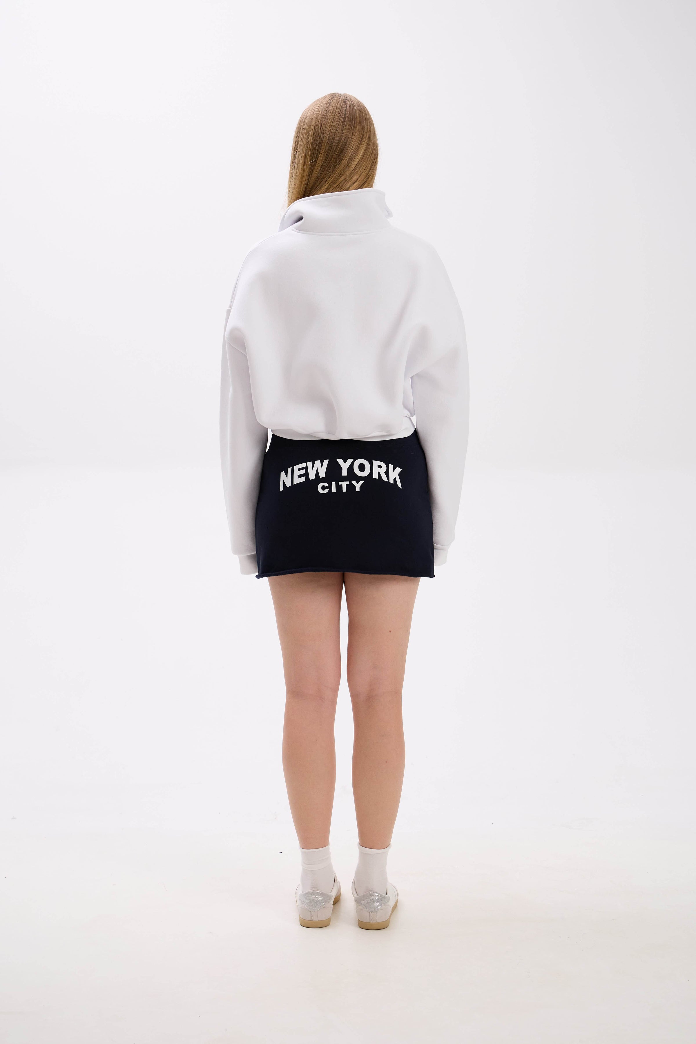 Person wearing a white hoodie and black skirt with 'New York City' text on a white background