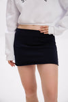 Person wearing a black mini skirt and white sweatshirt on a plain background