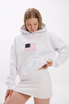 Close-up of model in a white hoodie with front patch detail, paired with a white mini skirt.