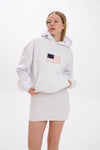 Model wearing a white hoodie with front patch detail, styled with a white mini skirt.
