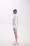 Side view of model wearing a white hoodie paired with a white mini skirt, socks, and sneakers.