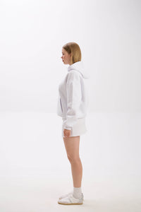 Side view of model wearing a white hoodie paired with a white mini skirt, socks, and sneakers.