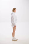 Side profile of model in a white hoodie paired with a white mini skirt, socks, and sneakers.