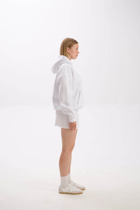 Side profile of model in a white hoodie paired with a white mini skirt, socks, and sneakers.
