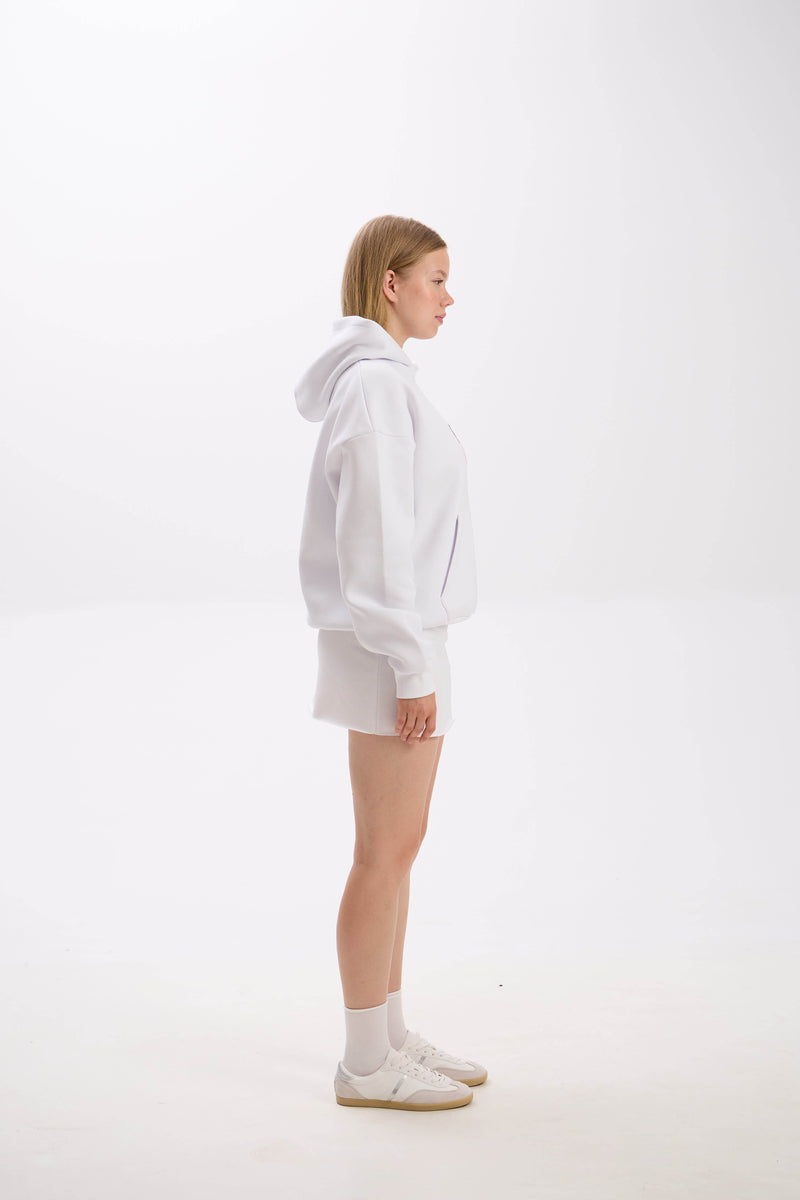 Side profile of model in a white hoodie paired with a white mini skirt, socks, and sneakers.