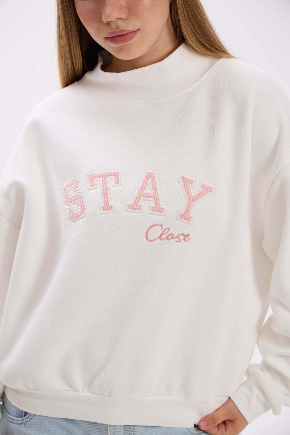 White sweatshirt with pink text worn by a person, on a plain background