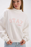 Person wearing a white sweatshirt with 'Stay Close' text in pink on a plain background