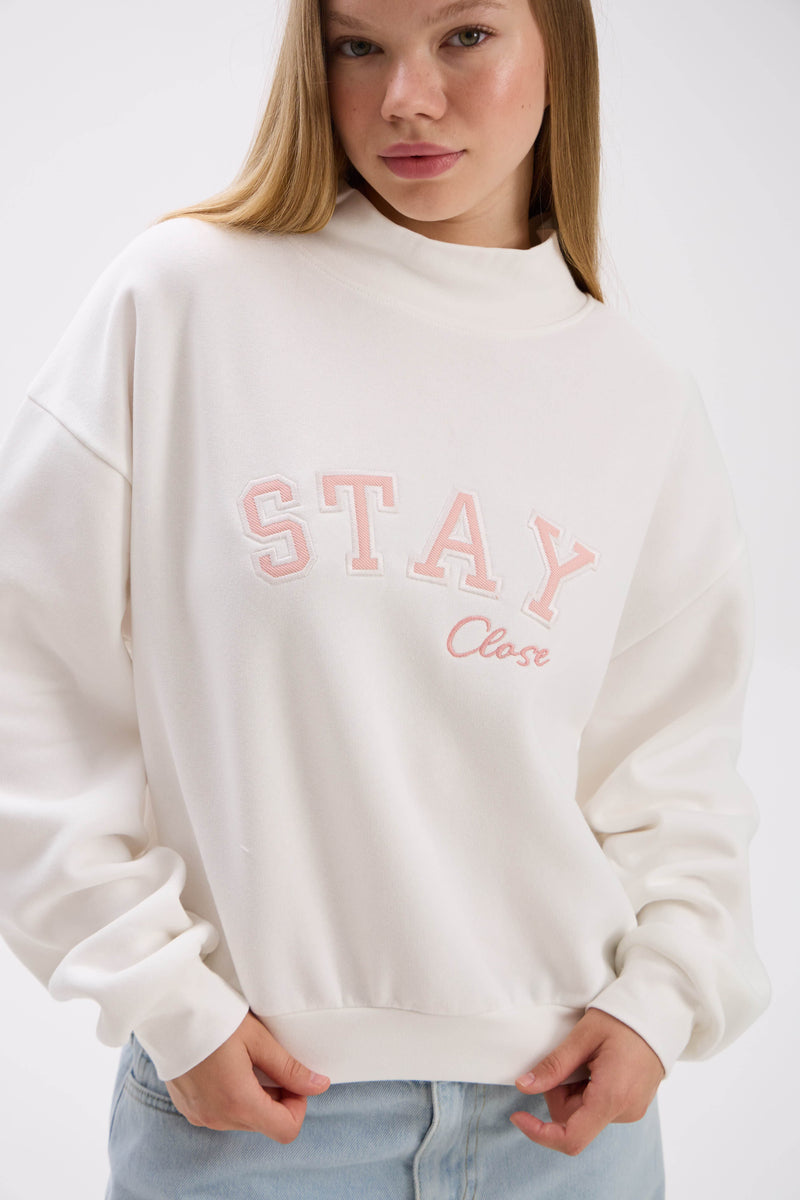 Person wearing a white sweatshirt with 'Stay Close' text in pink on a plain background