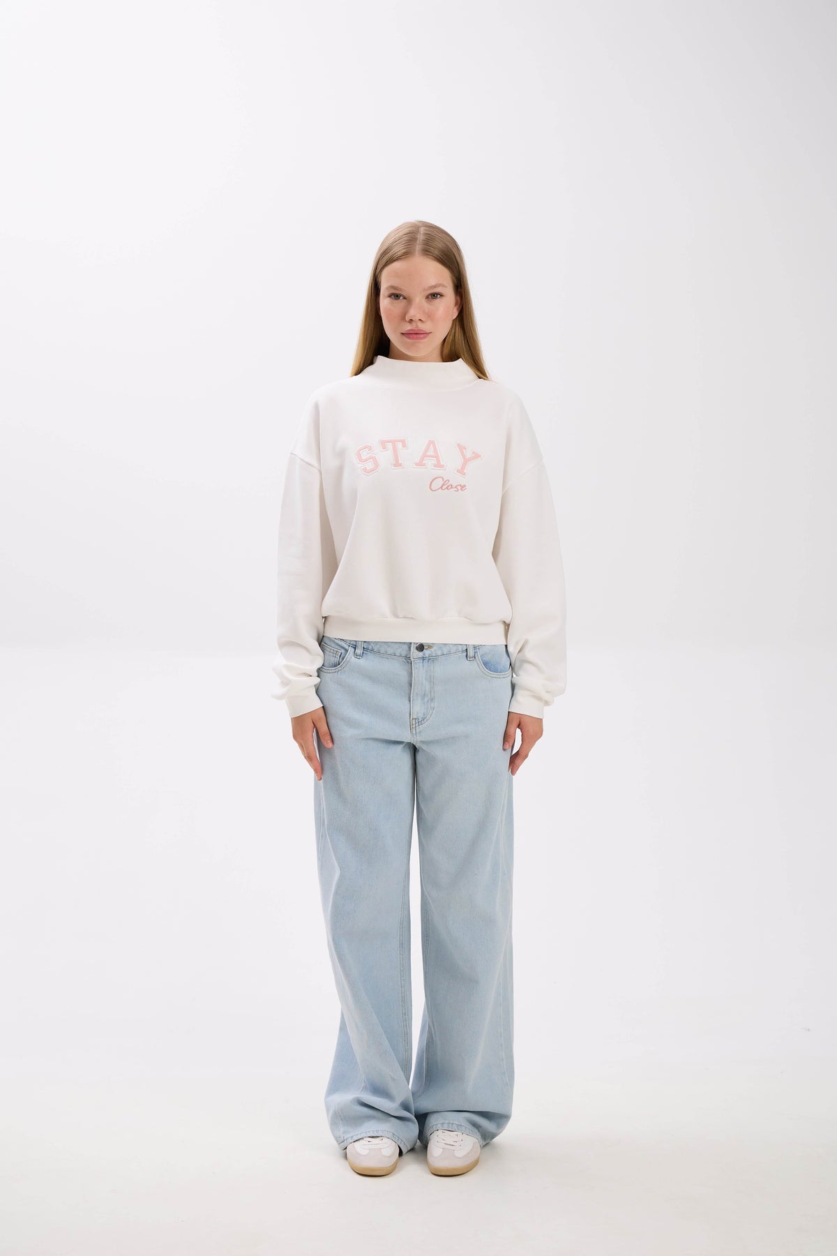 Person wearing a white sweatshirt with text and light blue jeans on a white background