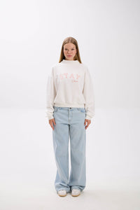 Person wearing a white sweatshirt with text and light blue jeans on a white background