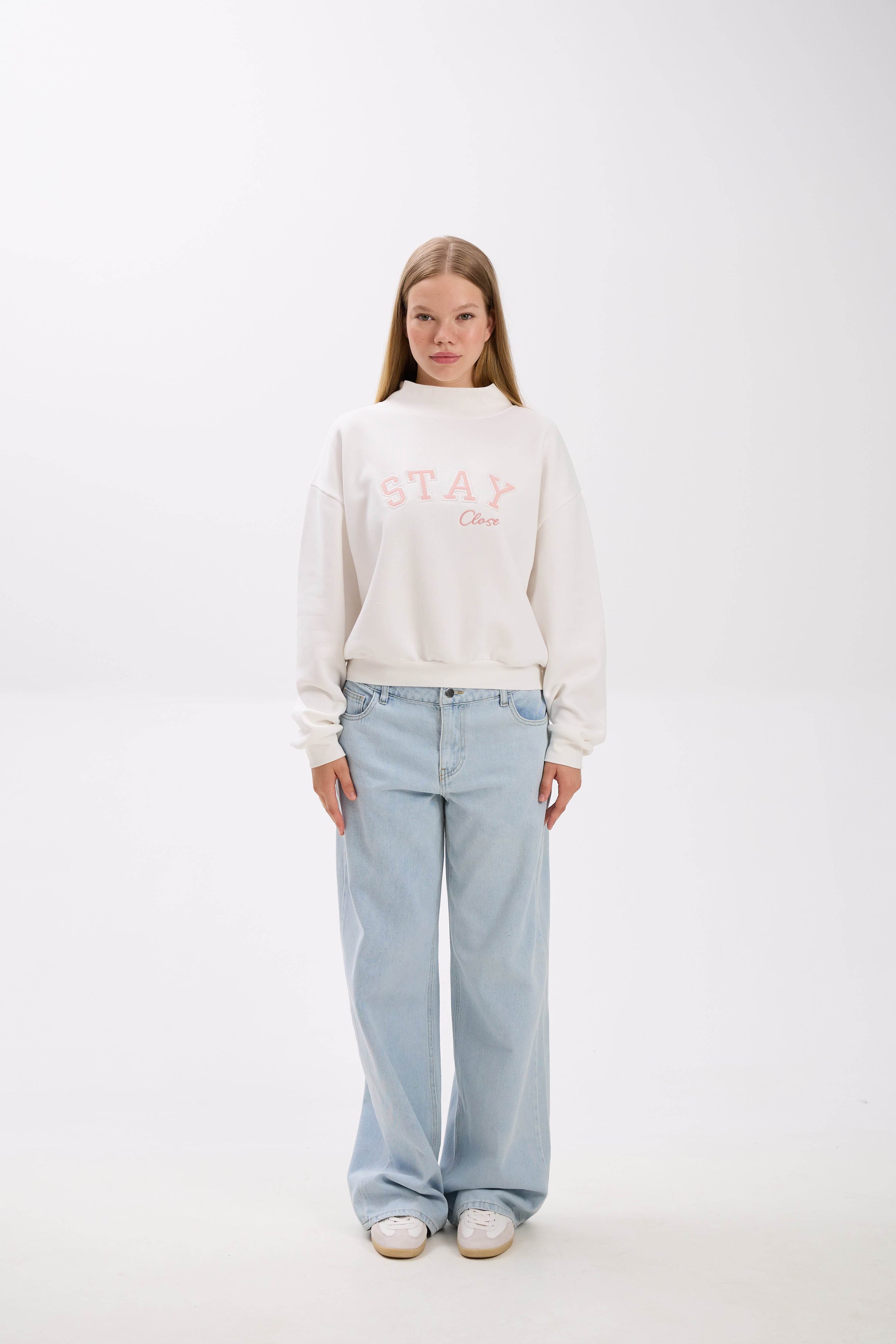 Person wearing a white sweatshirt with text and light blue jeans on a white background