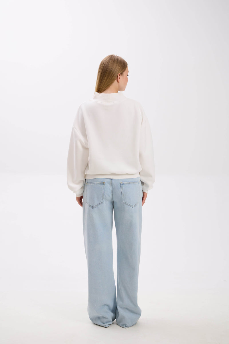 Person wearing a white sweater and light blue jeans on a white background