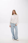 Person wearing a white sweater with text and light blue jeans on a white background