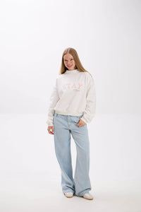 Person wearing a white sweater with text and light blue jeans on a white background