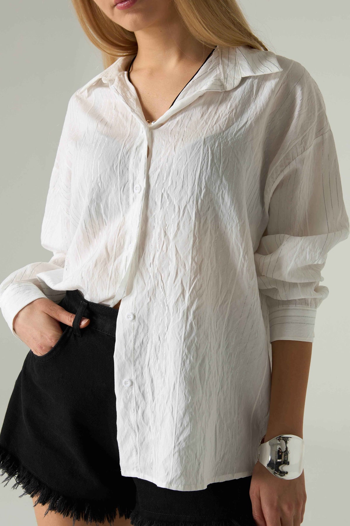 Person wearing a white textured shirt with rolled-up sleeves and black shorts on a plain background.