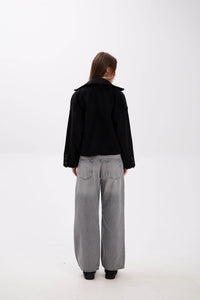 Person wearing a black jacket and gray pants on a white background