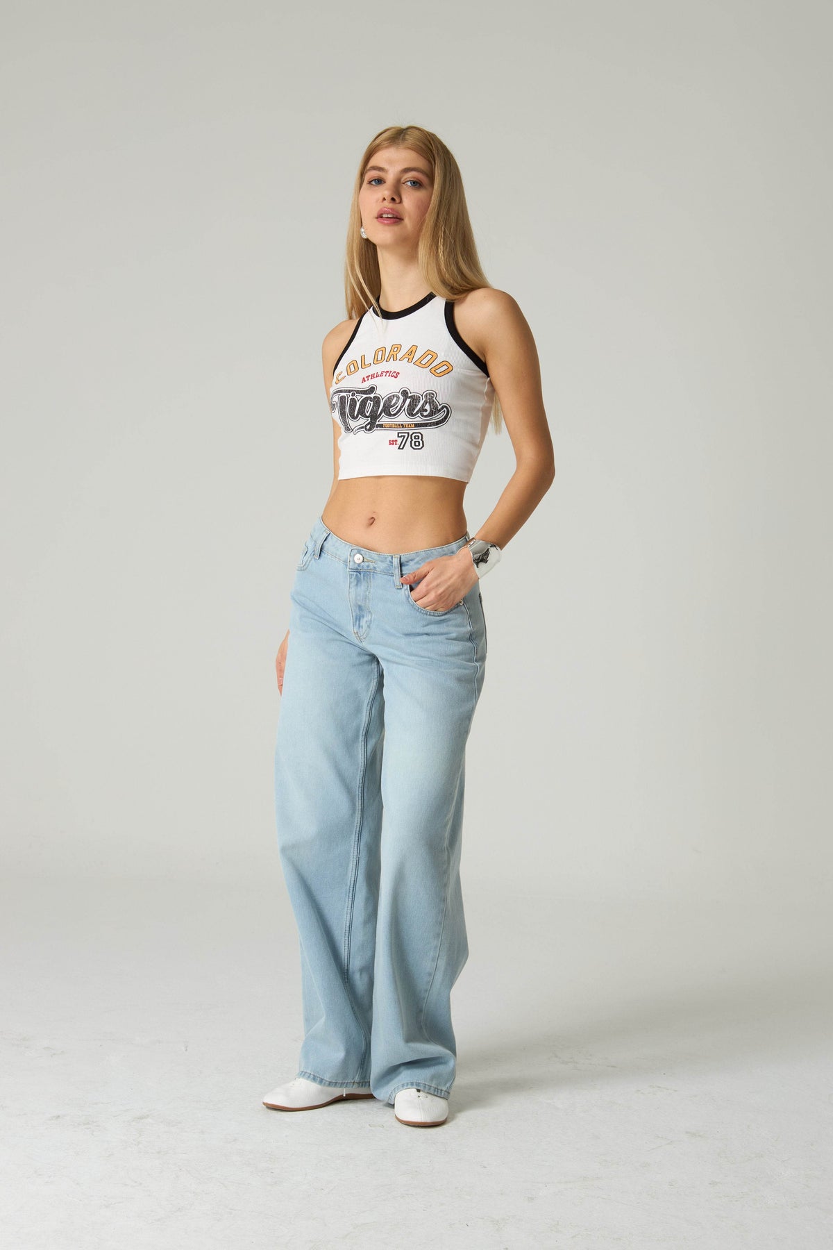 Woman wearing a white tank top with 'COLORADO Tigers' text and light blue jeans on a plain background.