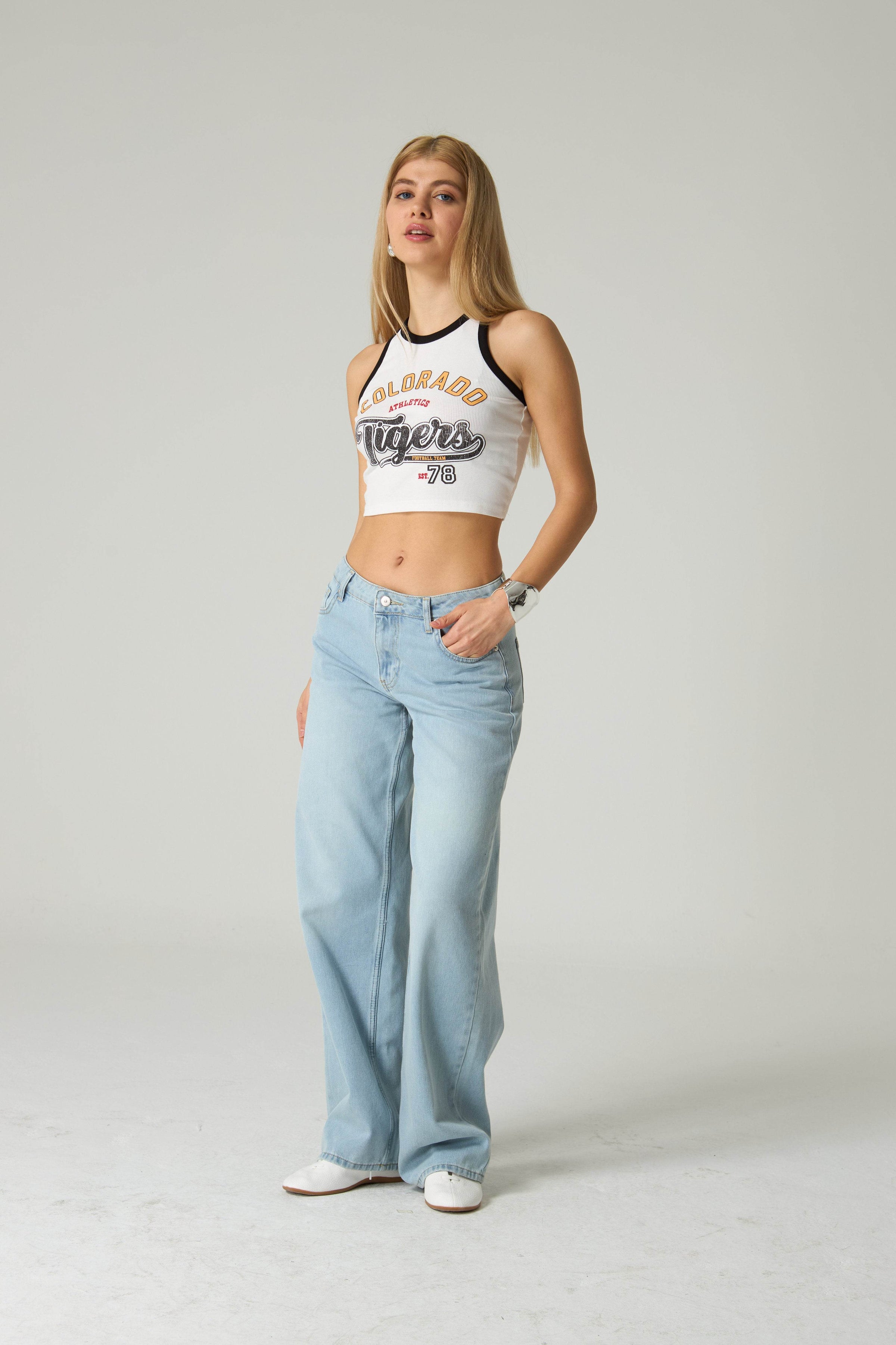Woman wearing a white tank top with 'COLORADO Tigers' text and light blue jeans on a plain background.