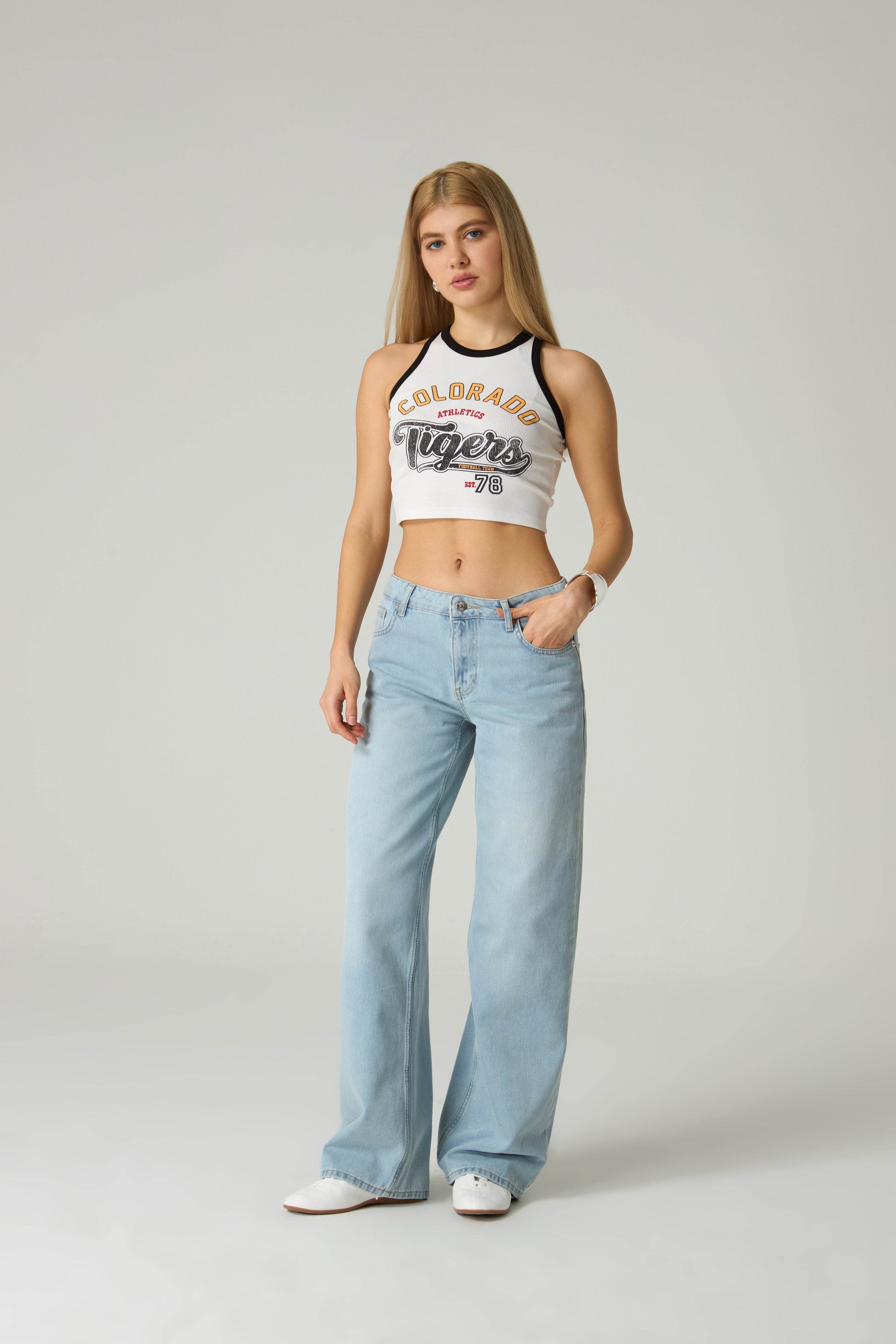 Woman wearing a white tank top with 'Colorado Tigers' text and light blue jeans on a plain background.