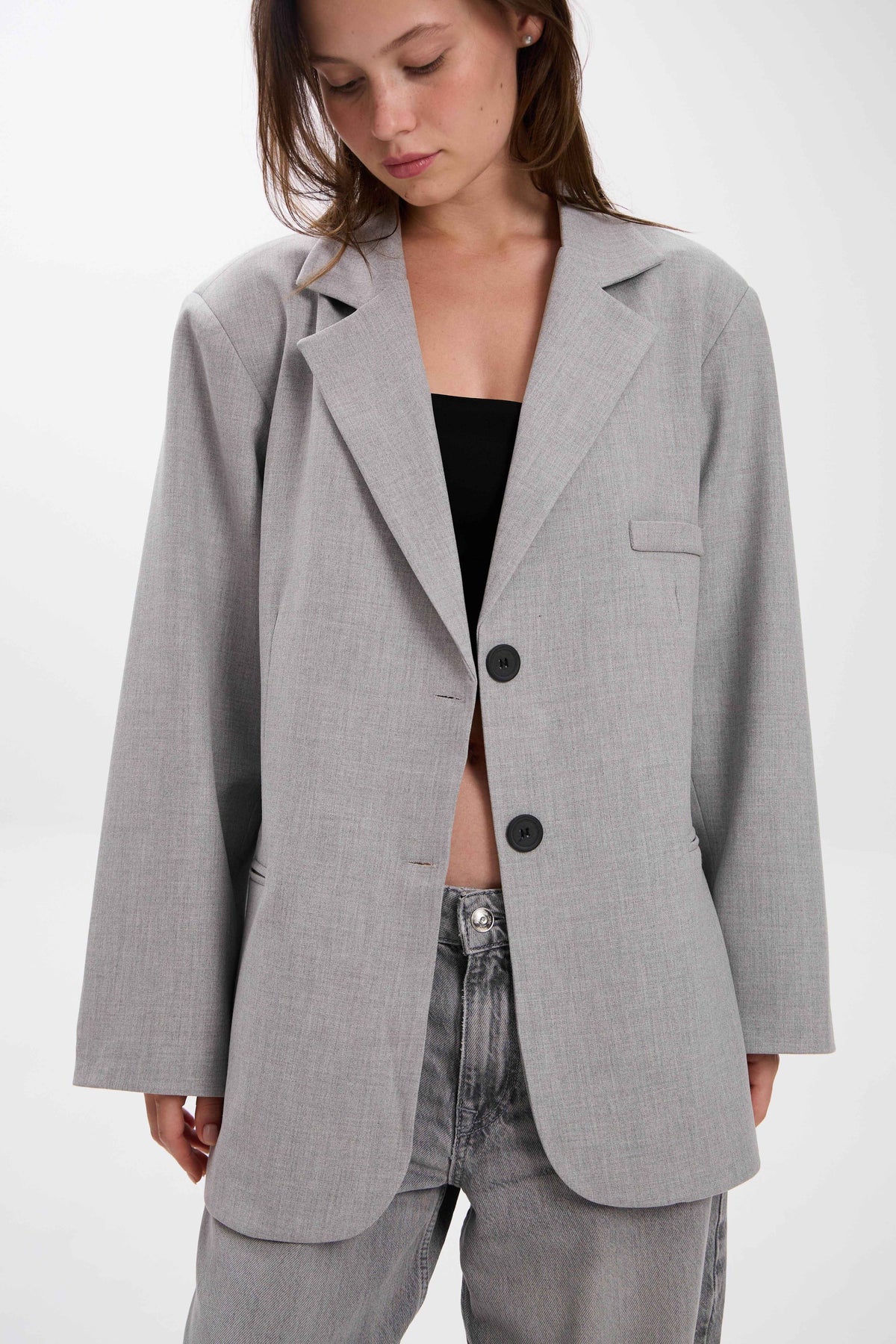 Person wearing a gray blazer over a black top and jeans on a white background.