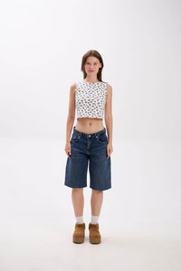 Woman wearing a patterned top and denim shorts on a white background.